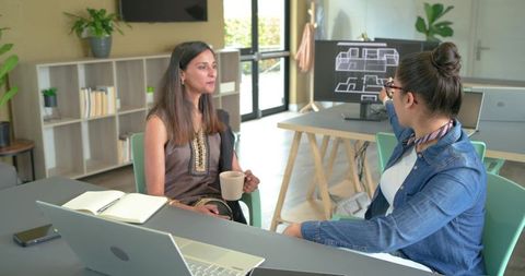 Female coworkers collaborating and pointing at digital floor plan in modern office