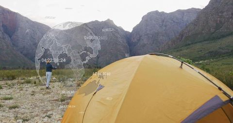 Solo camper walking toward mountain pass with yellow tent and ar globe overlay