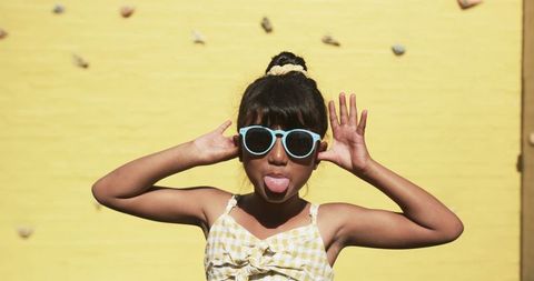 Playful Young Girl Sticking Tongue Out Against Yellow Background
