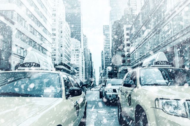 Yellow taxis driving through an urban city street during a heavy snowstorm. Skyscrapers lining the street show modern architecture covered in snow. Snowflakes falling rapidly create a wintry atmosphere and highlight challenging weather conditions. Ideal for depicting urban hustle in winter, transportation in harsh weather, or city life during cold seasons.