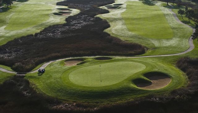 Aerial putting green with flag, bunkers and marshland fairways on coastal links