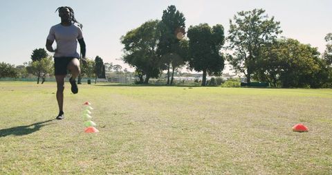 Performing agility drill sprinting through cone markers on sunny outdoor training field