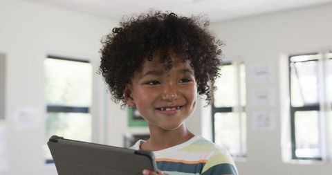 Smiling teenage student holding tablet in bright classroom learning technology and curiosity