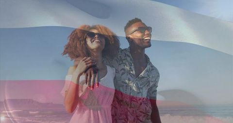 Young couple strolling on sunlit beach wearing sunglasses with colorful flag overlay