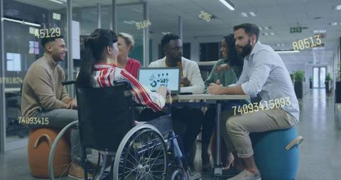 Collaborating diverse team reviewing data analytics around laptop with wheelchair inclusion