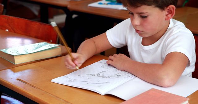 Young boy attentively writing in his notebook at a classroom desk. Ideal for educational resources, learning materials, school project presentations, and educational articles emphasizing childhood education and development.