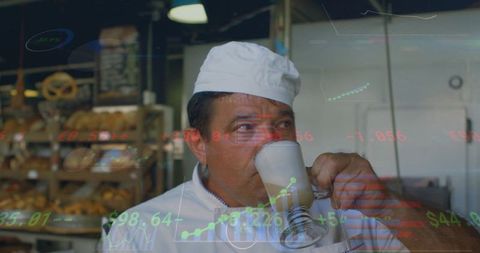 Baker sipping latte and pausing in bakery among bread racks with stock chart overlays