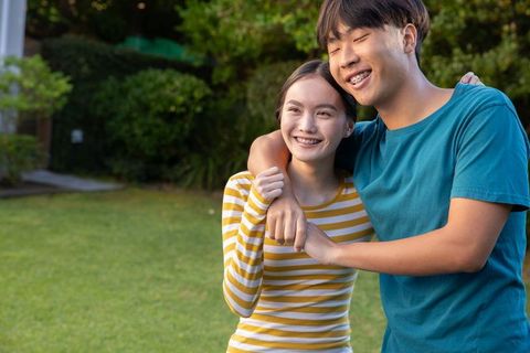 Cheerful Asian Couple Smiling on Grass in Sunlit Garden