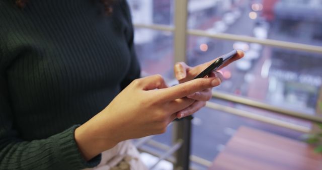 Person using smartphone near office window with urban view - Download Free Stock Images Pikwizard.com