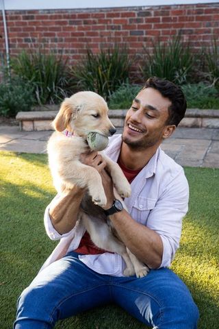 Happy man playing with golden retriever puppy outdoors