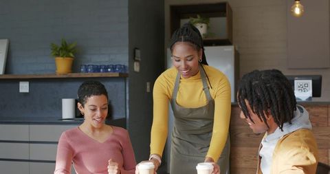 Smiling barista serving to-go coffee to diverse friends at cozy modern neighborhood cafe