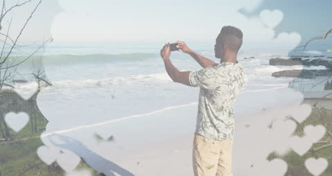 Man on Beach Taking Selfie Surrounded by Romantic Hearts