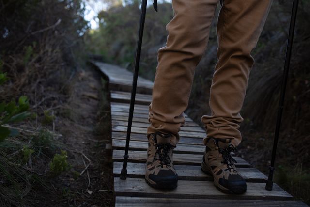 Front view low section of a senior Caucasian man enjoying time in nature, hiking in mountains, walking on a wooden footpath in hiking boots and with Nordic walking sticks.