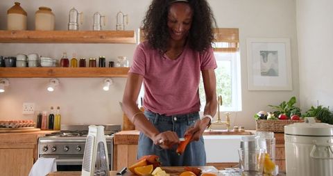 African american woman preparing fresh orange juice in kitchen