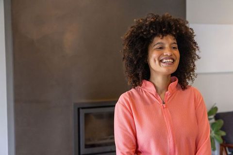 African american woman smiling in coral zip-up jacket by modern fireplace interior