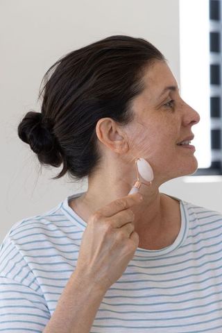 Mature woman massaging jawline with rose quartz facial roller for glowing skincare routine