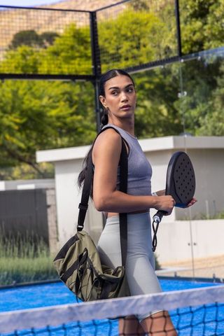 Athlete carrying paddle and olive gym bag on blue outdoor court in activewear