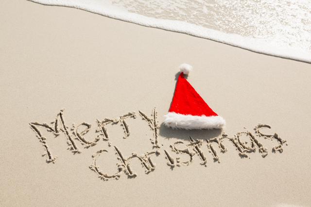 Merry Christmas written on sand with santa hat at beach