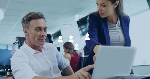 Female manager pointing at laptop while collaborating with male colleague in modern office