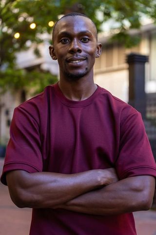 Confident african american man standing arms crossed in urban courtyard at golden hour