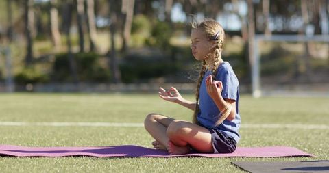School-age girl practicing meditation on sunlit soccer field during outdoor yoga session