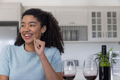 Smiling woman in modern kitchen with red wine glasses