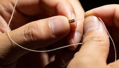 Closeup hands threading tiny seed beads on thread creating delicate handmade jewelry