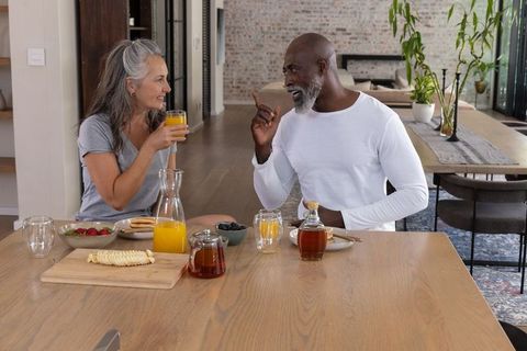 Multiracial couple enjoying morning breakfast with orange juice in rustic modern kitchen