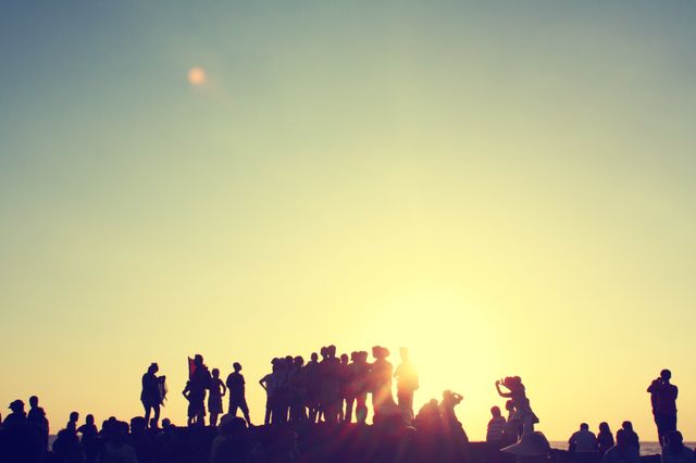 Large group of people silhouetted against a setting sun. Ideal for concepts of friendship, community, gatherings, vacations, and outdoor activities.