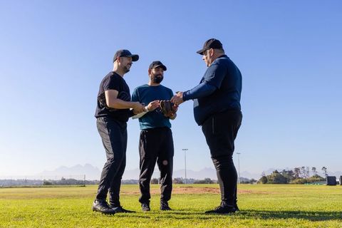 Three men exchanging baseball glove during coaching huddle, teamwork training outdoors