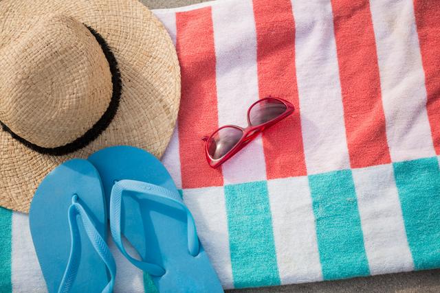 Straw hat, blue flip flop and sunglasses kept on beach blanket at tropical beach
