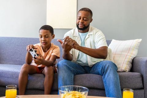 African american father coaching son on video game controller during cozy family gaming