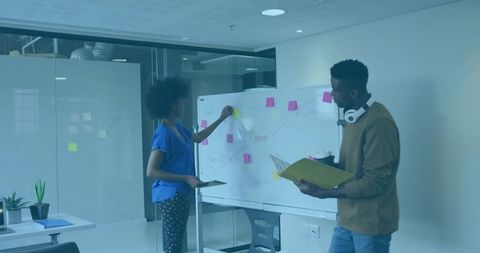 Team brainstorming at whiteboard placing sticky notes and mapping ideas in office workshop