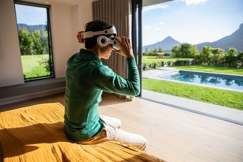 Asian man adjusting vr headset in modern bedroom opening to pool and mountain view