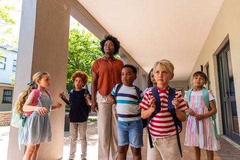 Elementary students and african american teacher walking school walkway carrying backpacks