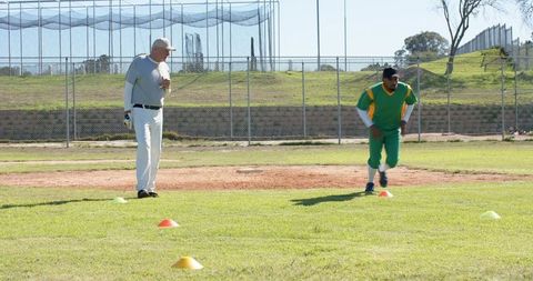Senior coach coaching player running agility drill on baseball field outdoors