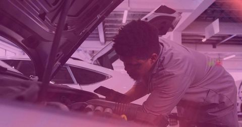 Mechanic inspecting engine bay with smartphone under raised hood in garage with purple lighting