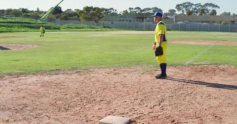Infielder standing ready on dusty baseball infield in bright yellow uniform near base