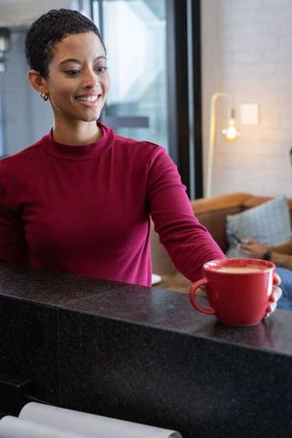 African american barista serving latte at cafe counter wearing burgundy sweater