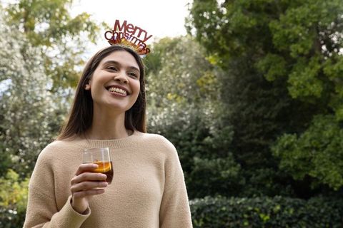 Asian woman wearing merry christmas headband celebrating outdoors with drink