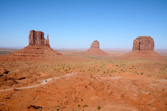 This image shows an iconic landscape of Monument Valley with prominent red rock formations under a clear blue sky. Ideal for uses in travel and tourism promotions, geographical studies, educational content, outdoor adventure advertisements, and nature documentaries.
