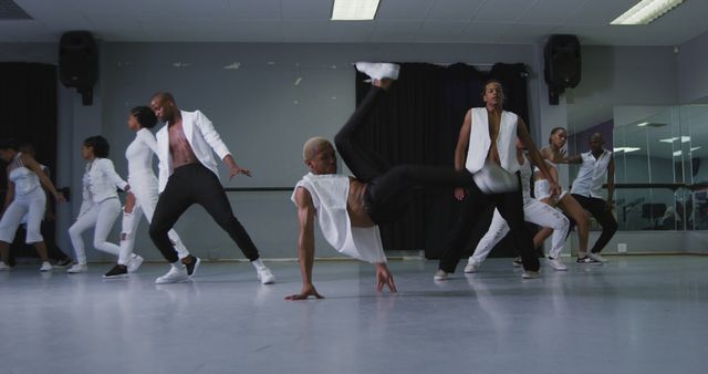 This stock image showcases a diverse group of dancers performing a high-energy hip hop routine in a studio. The performers are dressed in stylish, coordinated outfits as they execute dynamic moves including breakdancing. This image captures the essence of creativity, teamwork, and urban culture. Ideal for use in marketing materials related to dance studios, urban culture events, music videos, and fitness programs.