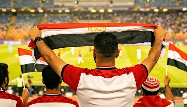 Egyptian football fans cheering with flag scarf in stadium under floodlights at night
