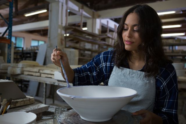 Female potter decorating bowl with paint brush in pottery workshop