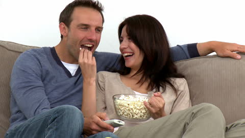 Happy Couple Enjoying Popcorn While Watching TV at Home