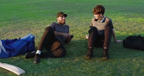 After-practice friends laughing on grass sharing phone clip outdoor leisure and bonding