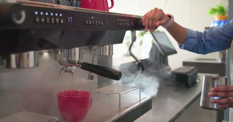 Barista steaming milk and pulling espresso shot with red cup on espresso machine