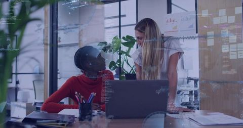 Colleagues collaborating over laptop in modern open-plan office with glass walls and plants