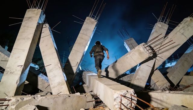 Backpacked explorer walking on concrete beam through collapsed industrial rubble at night