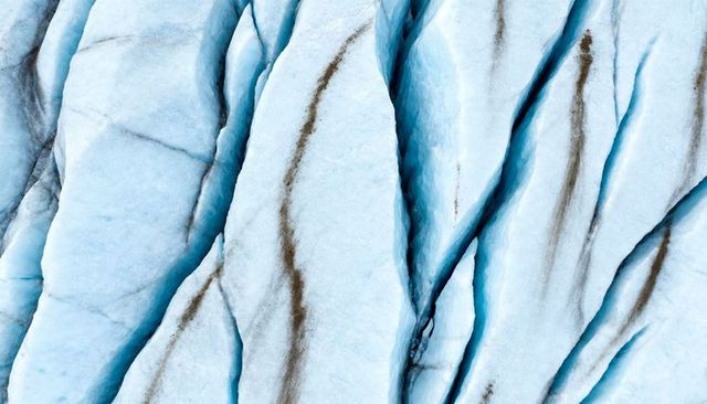 Aerial abstract revealing blue glacier crevasses, ice ridges and dark moraine streaks